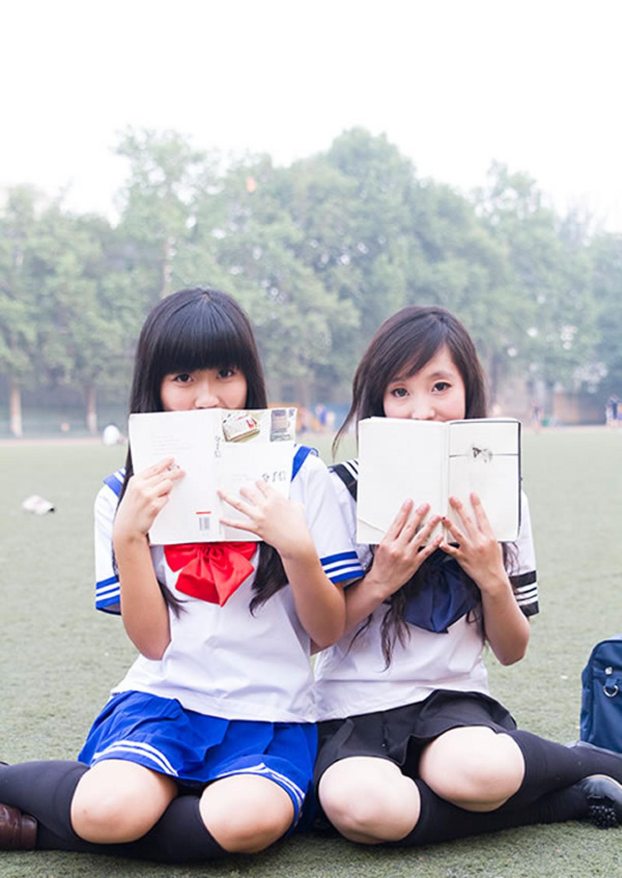 姊妹校服篇姐妹坐在操场同时用书遮住自己的半边脸正面照
