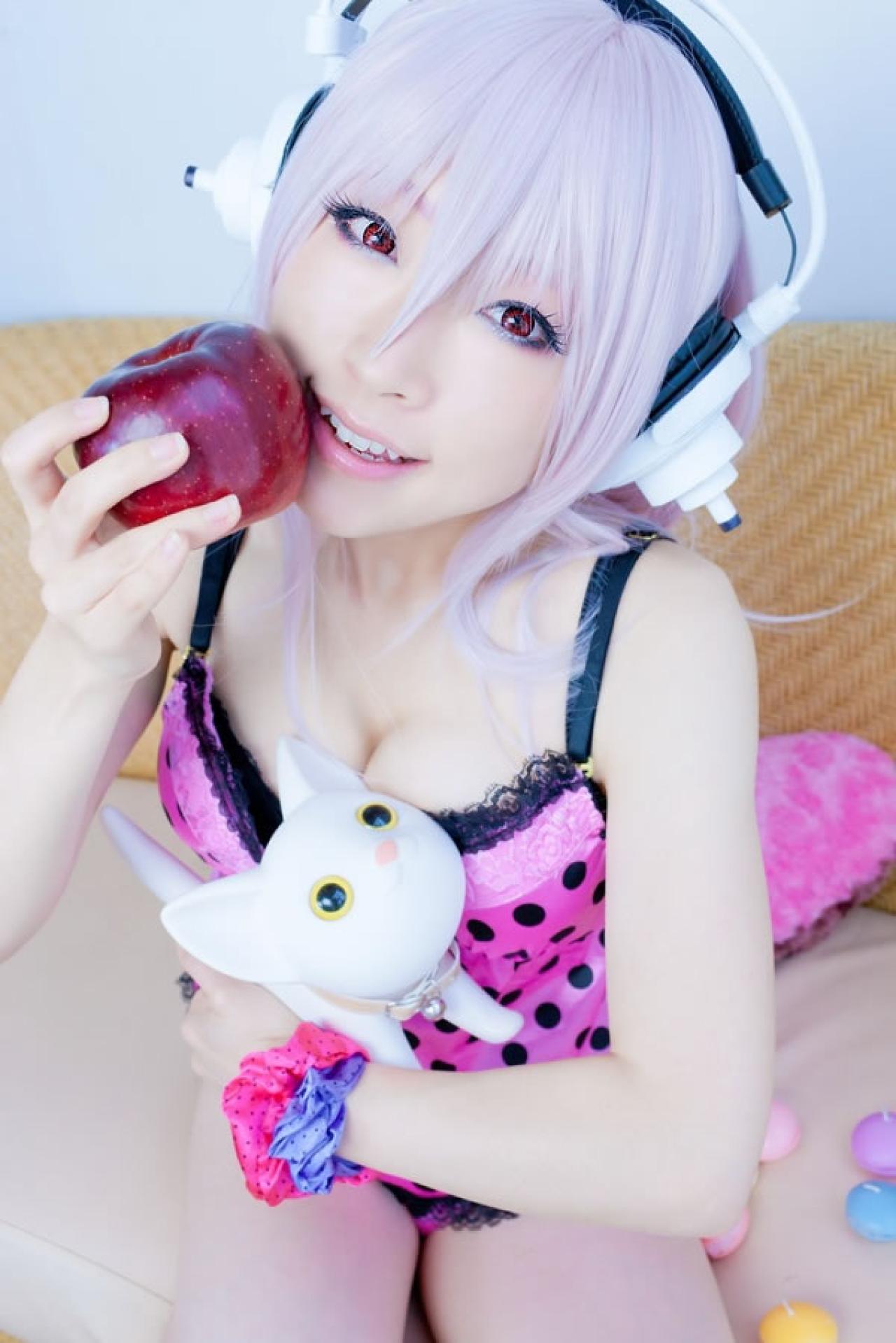 K@ori扮演超级索尼子戴着耳机穿着粉色吊带将苹果靠在嘴角，怀抱着小猫的样子