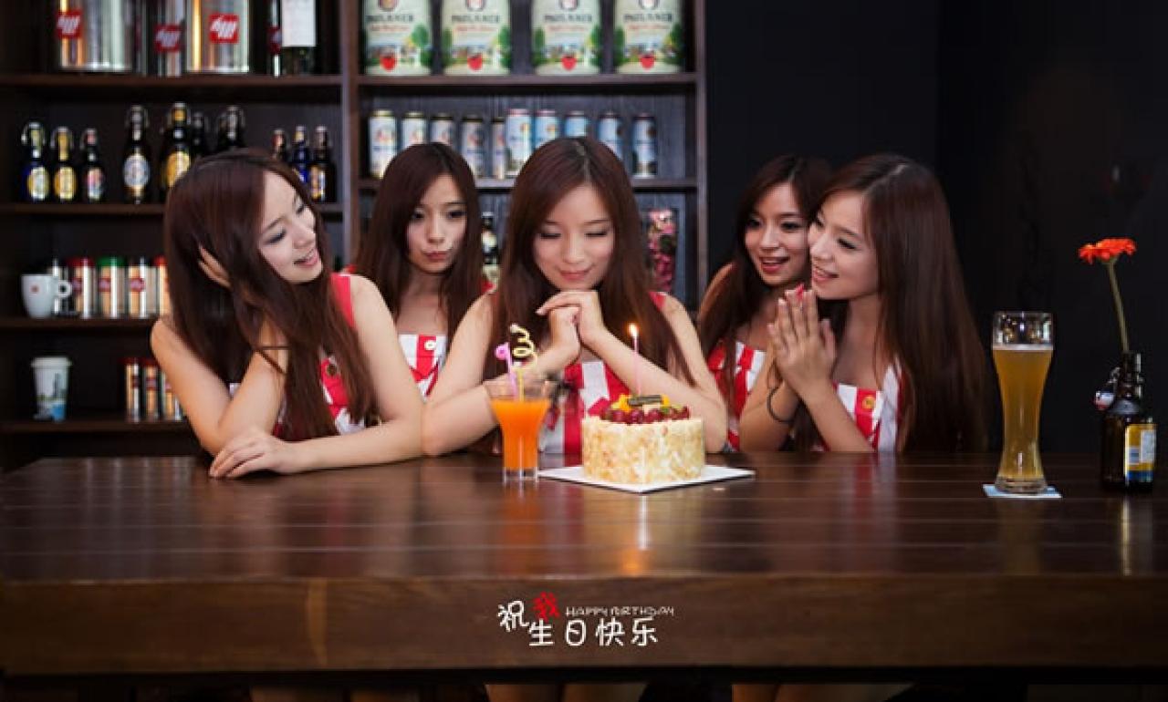 几位穿红色条纹衣裤的姑娘在酒吧生日聚会，过生日的姑娘面对蛋糕，双手合十，许下心愿