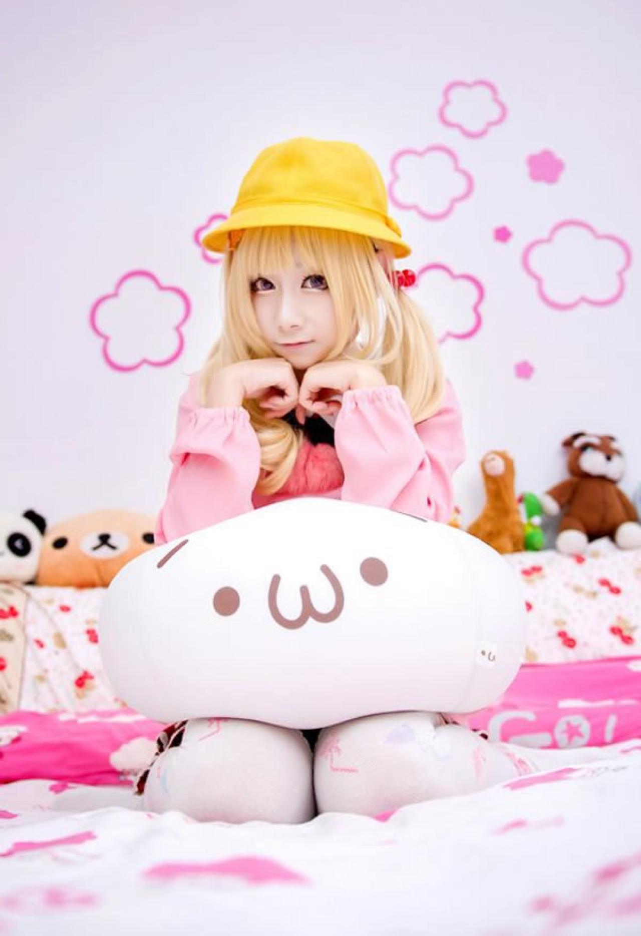 小甜幼稚园Cosplay穿着粉衣戴着黄帽，夹着抱枕跪坐在床上