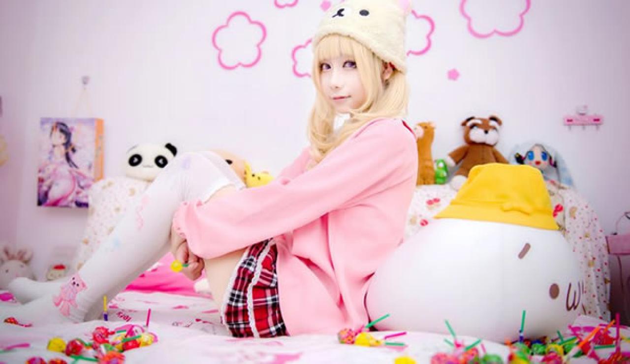 小甜幼稚园Cosplay穿着粉衣侧靠在嘟嘴抱枕上，床上洒满了棒棒糖