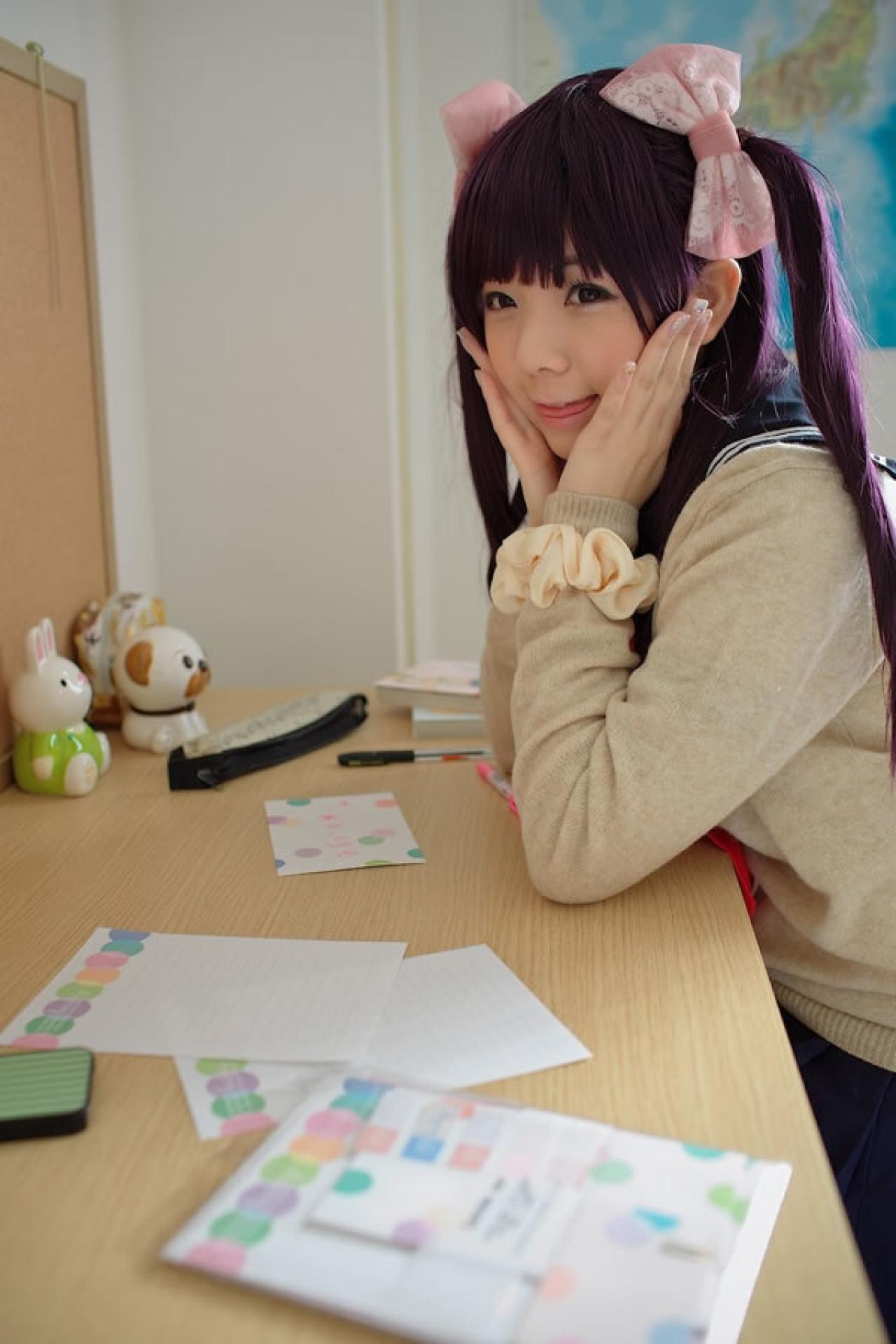 香坂ゆん扮演京野明日香身穿水手服和米色羊毛衫，双手捧着脸靠在桌子上吐舌卖萌