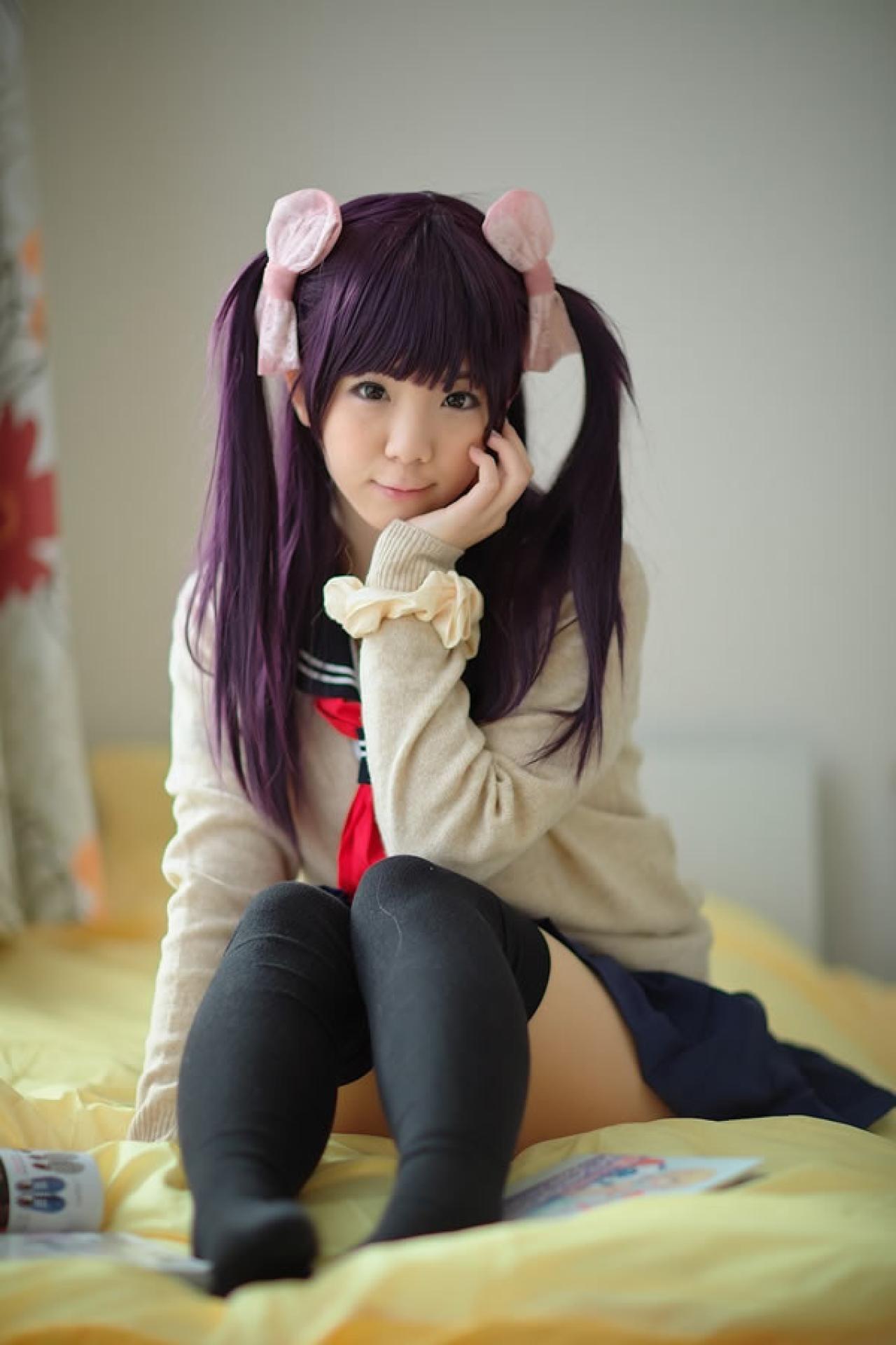 香坂ゆん扮演京野明日香身穿水手服和米色羊毛衫，坐在床上，单手扶着下巴正面