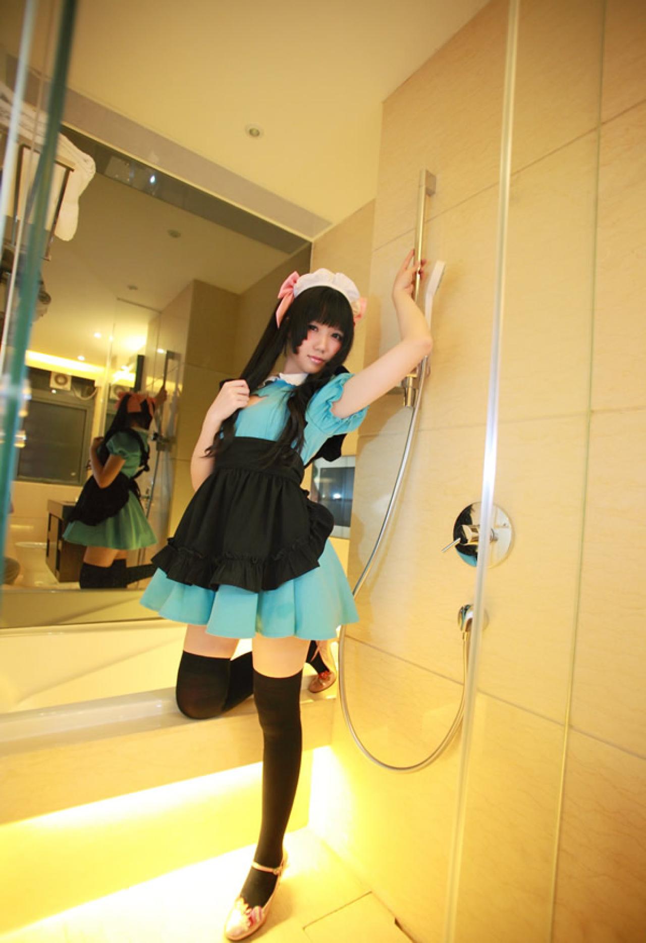 小米穿着绿色女仆装粉红发饰，把淋浴喷头放回原处，扶着栏杆站立摆拍