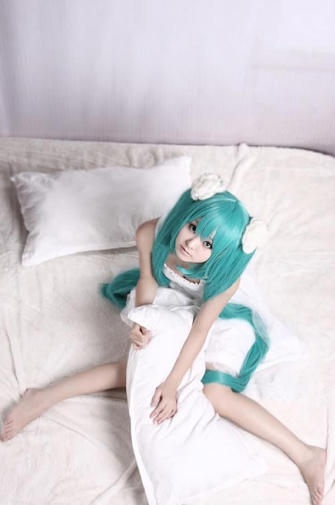 kuuya穿着白色睡衣扮演初音未来坐在床上，抱着枕头俯拍的样子