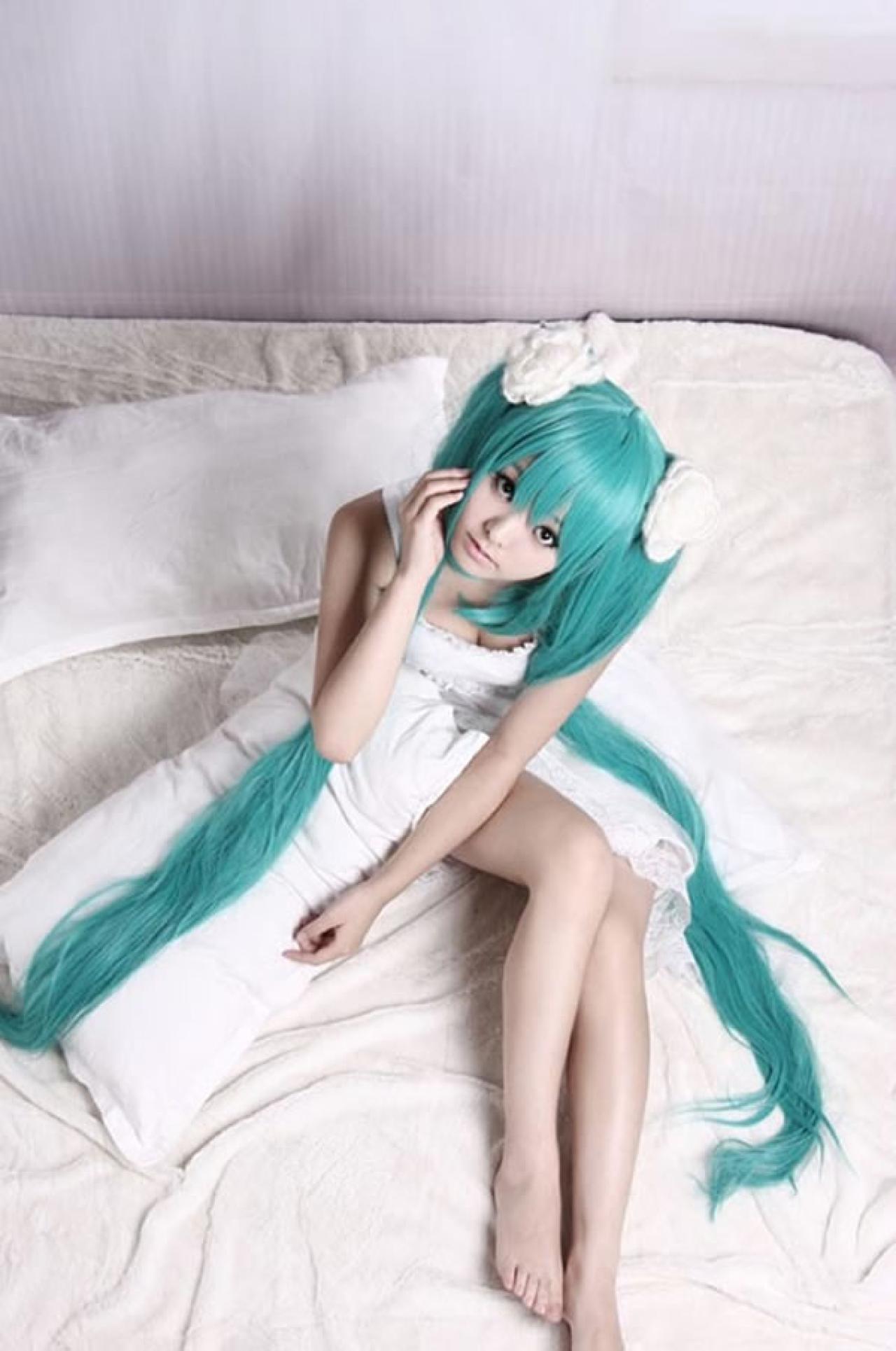 kuuya穿着白色睡衣扮演初音未来坐在枕头上，扶住脸颊的样子