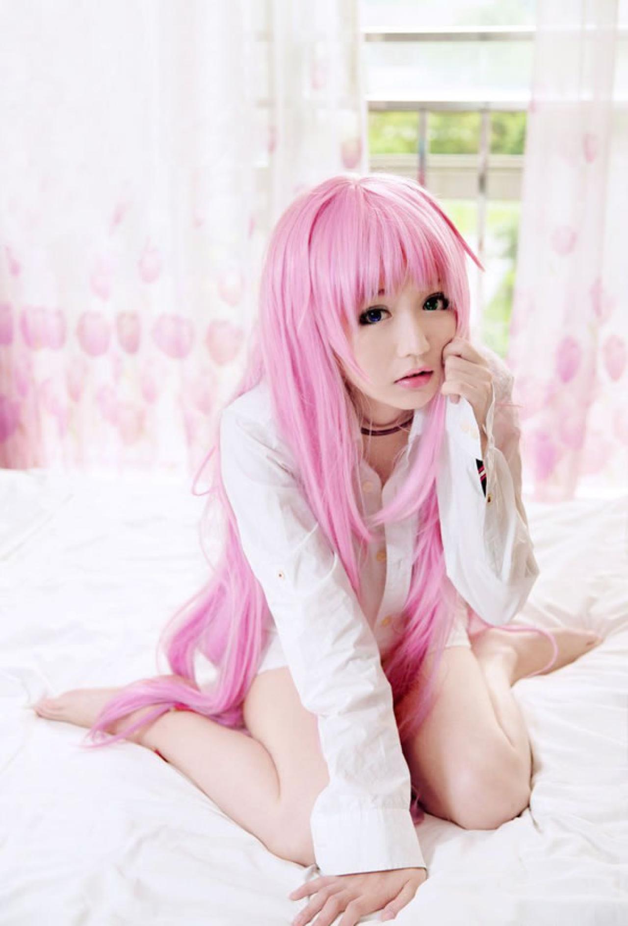 摆摆扮演《K》粉色猫娘，一手摸着脸颊，一手扶在床上的样子