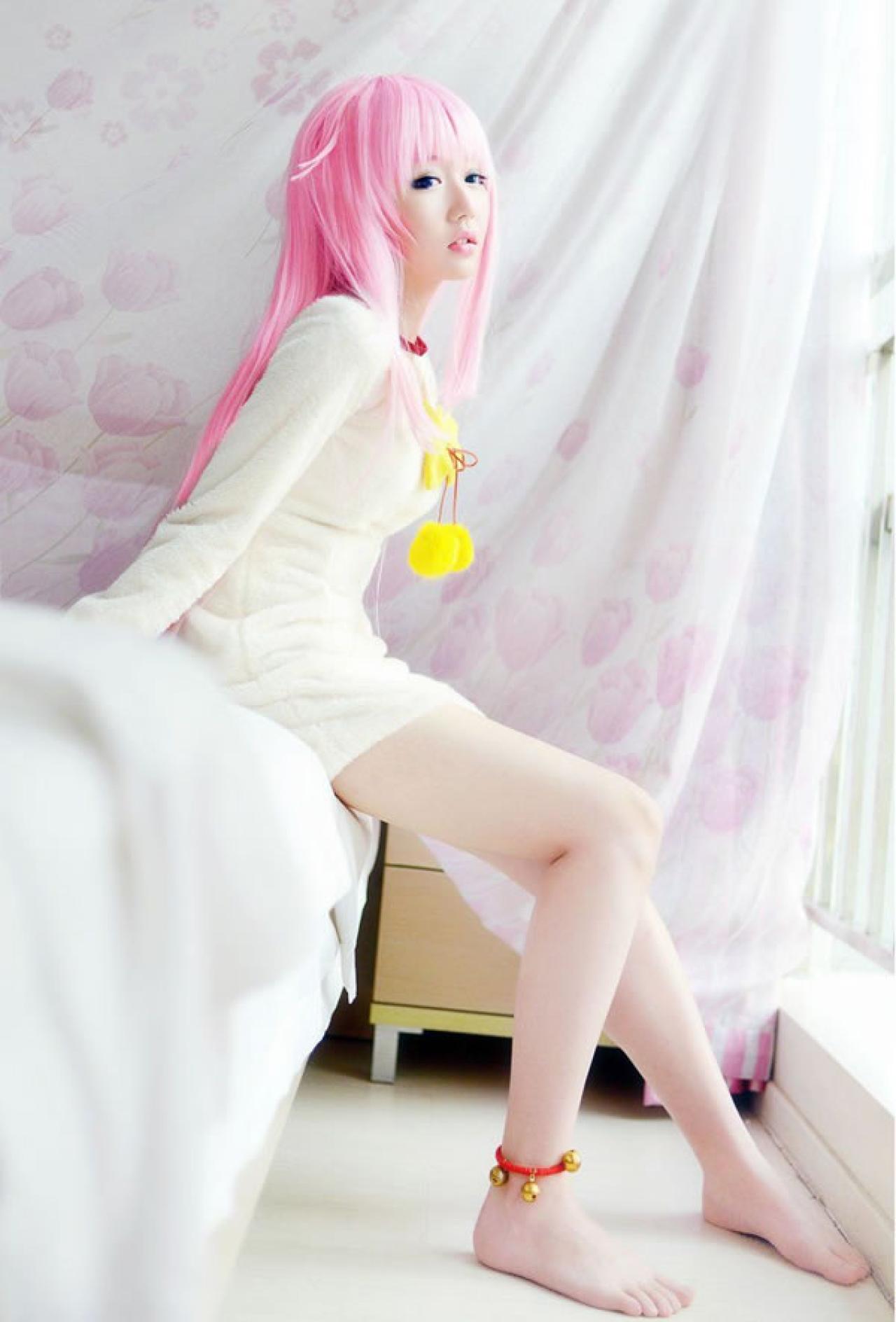 摆摆扮演《K》粉色猫娘，套着米色外套坐在床头的样子