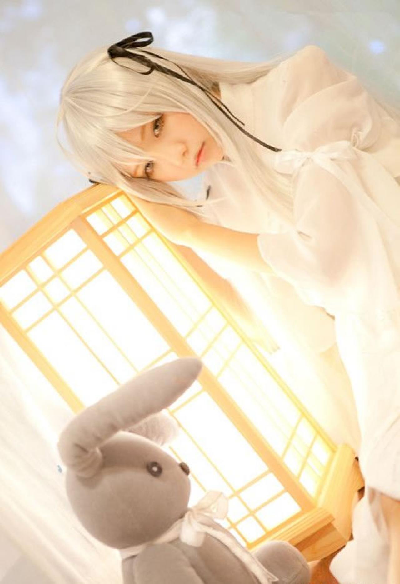 哀子扮演穹妹穿着白色连衣裙靠在木制灯箱上，看着兔子玩偶