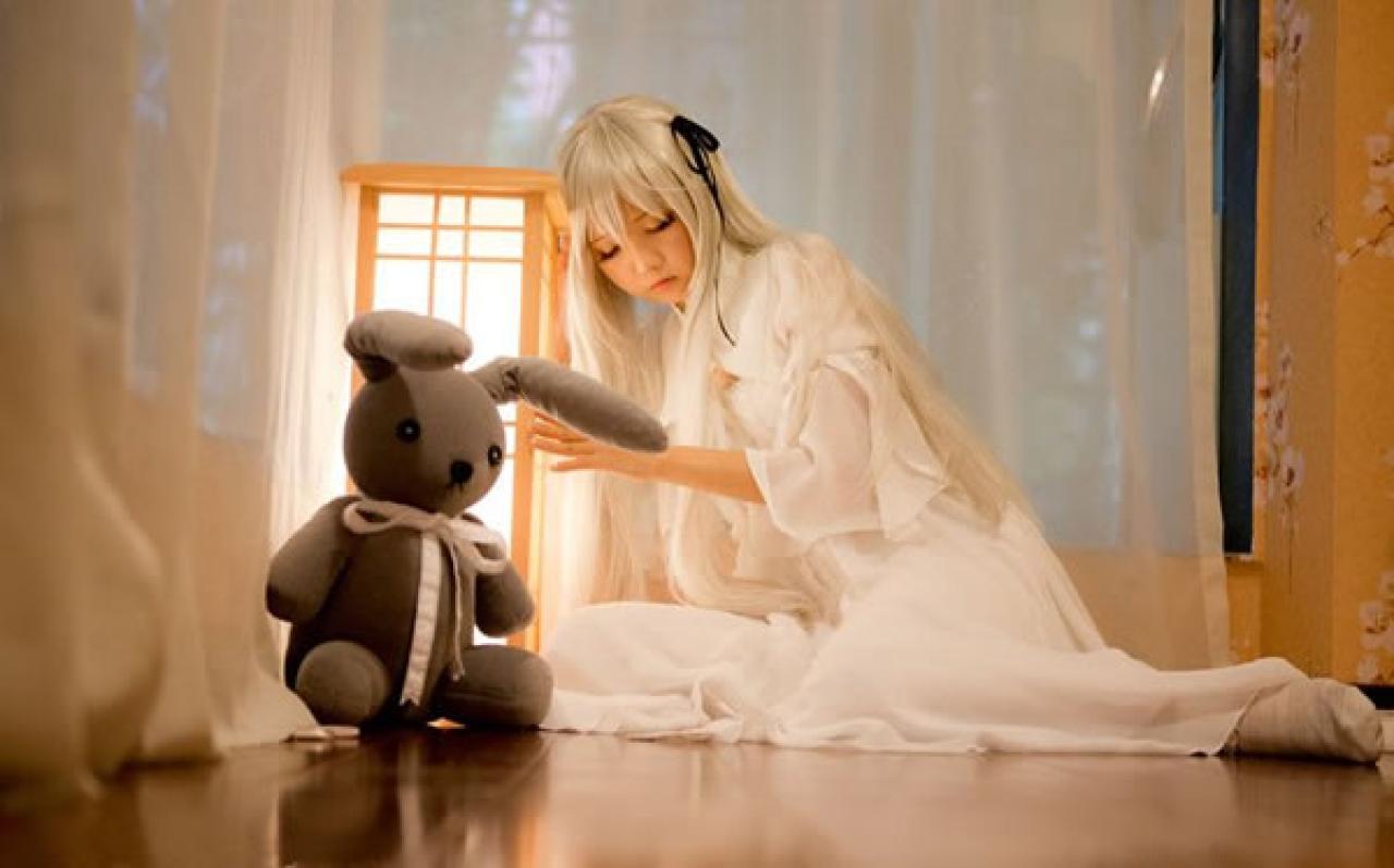 哀子扮演穹妹穿着白色连衣裙半跪在木地板上，头和身子轻轻依偎着木制灯箱