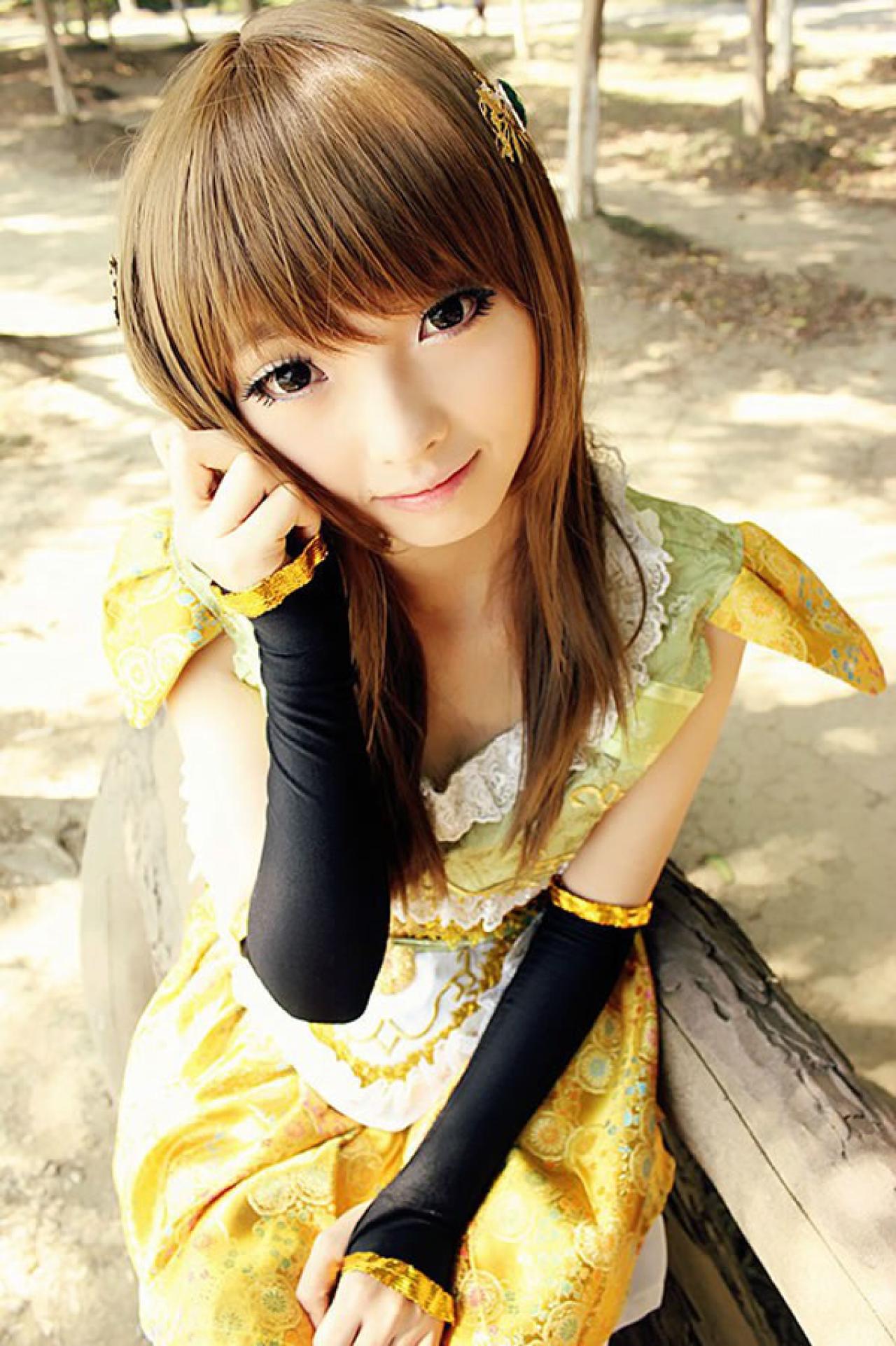 CC喵穿着黄色古装扮演小乔坐在枯木上，一手贴着脸，微笑的样子