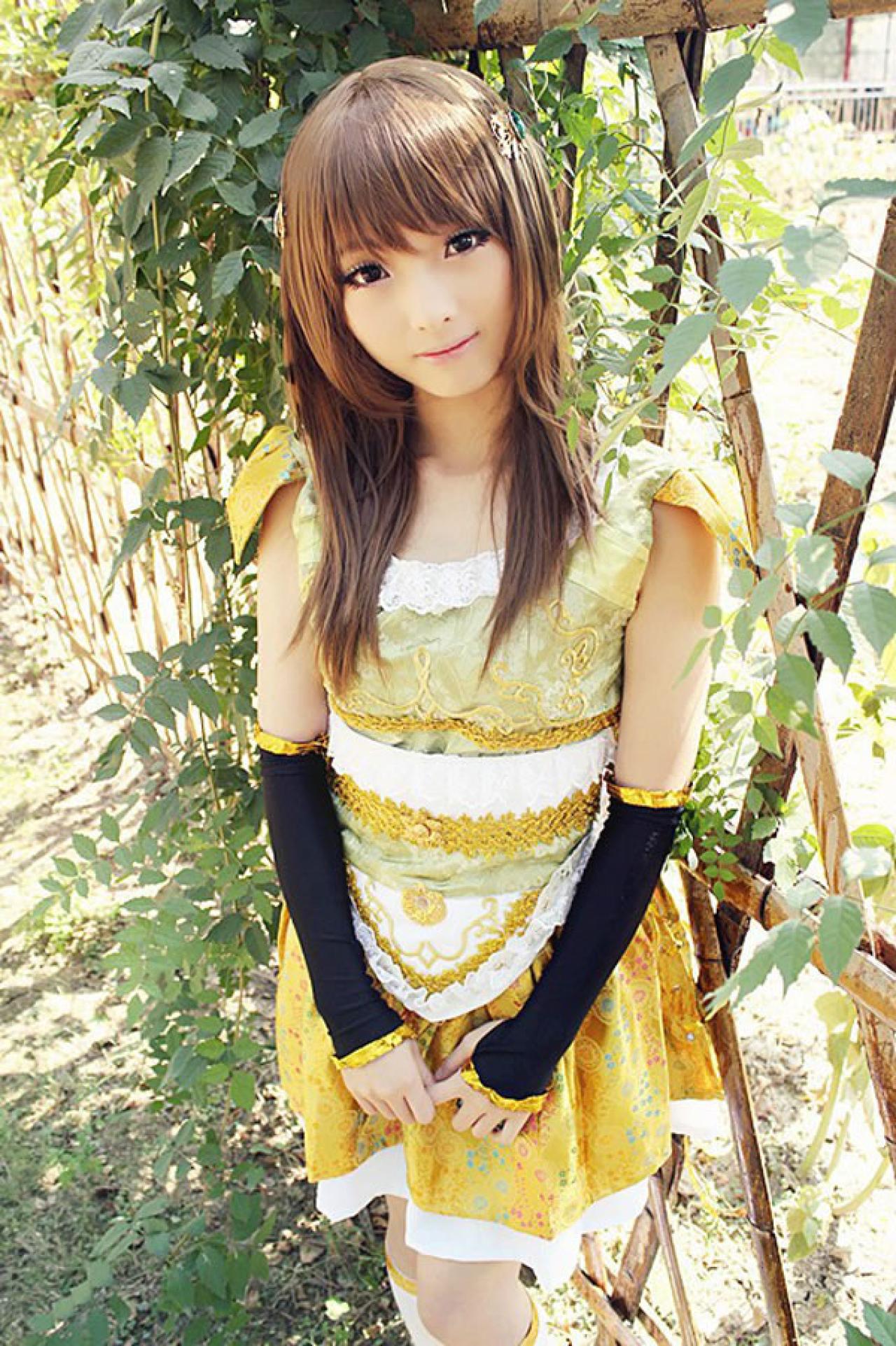 CC喵穿着黄色古装扮演小乔，一手拉着一手食指，站在爬满绿色爬山虎的栅栏外面