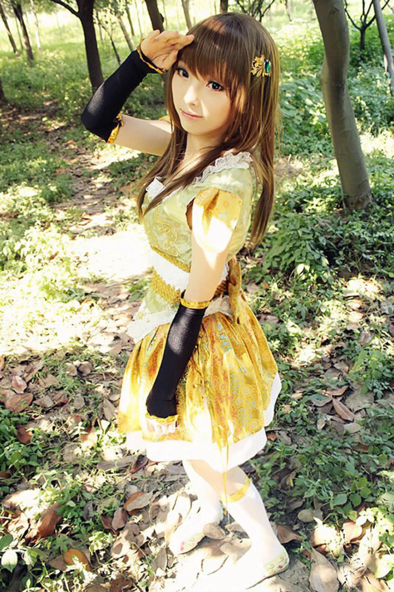 CC喵穿着黄色古装扮演小乔，在林中漫步，回头看镜头的同时，用手遮挡阳光