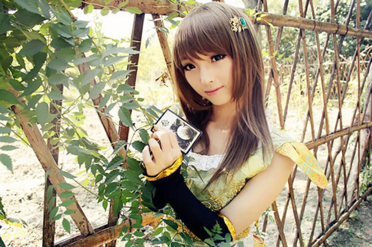 CC喵穿着黄色古装扮演小乔双手捧着一束爬山虎，放在身上，手里拿着一张三国杀卡牌