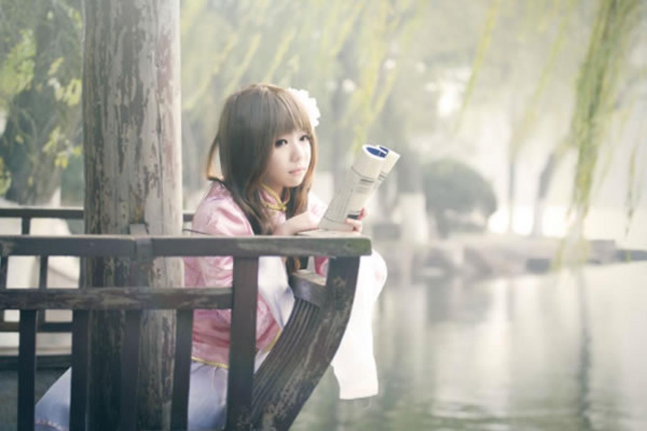 季_凋葬穿着粉衣扮演湾娘靠在亭子的长椅上看书的样子