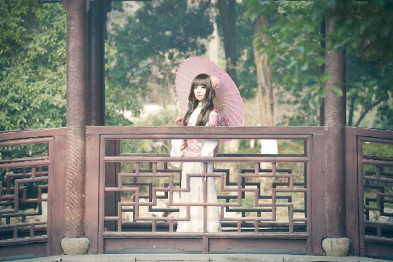 季_凋葬穿着粉衣扮演湾娘站在长廊上，撑着粉色油纸伞，看湖水的样子