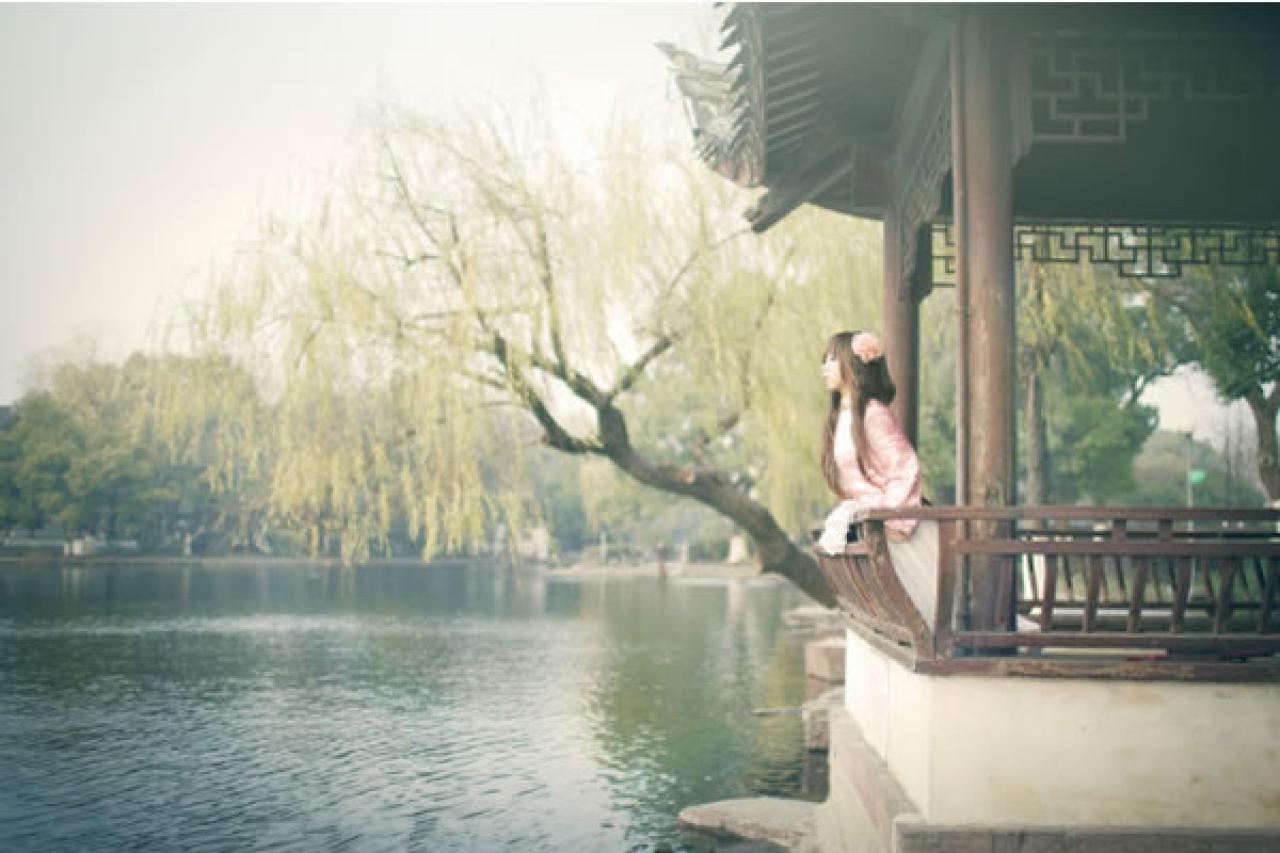 季_凋葬穿着粉衣扮演湾娘扶着长廊的扶手，前倾身体，望着湖面