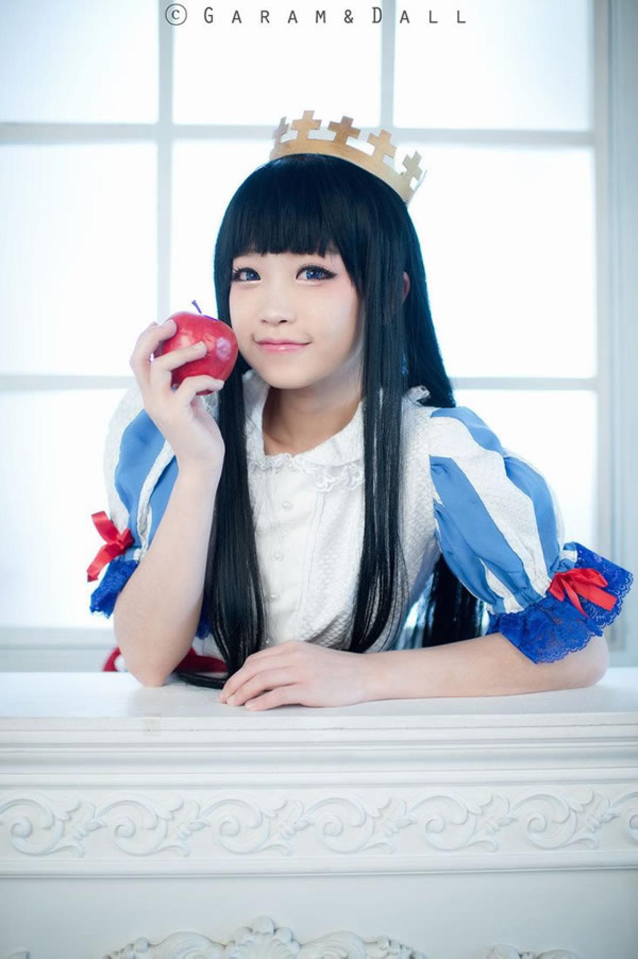 兔娘Tomia穿着蓝白洋装扮演白雪公主拿着苹果贴在脸庞，嘿嘿的笑着