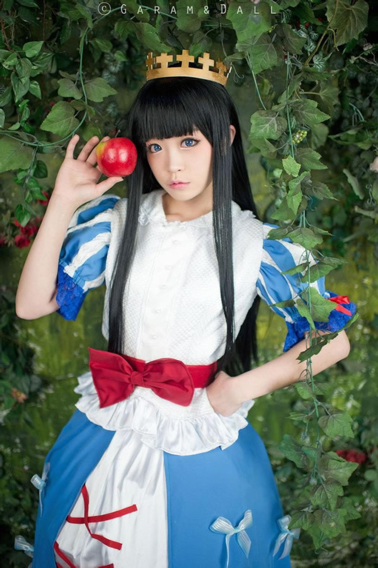 兔娘Tomia穿着蓝白洋装扮演白雪公主站在葡萄滕旁，一手叉腰，一手拿着苹果的站姿