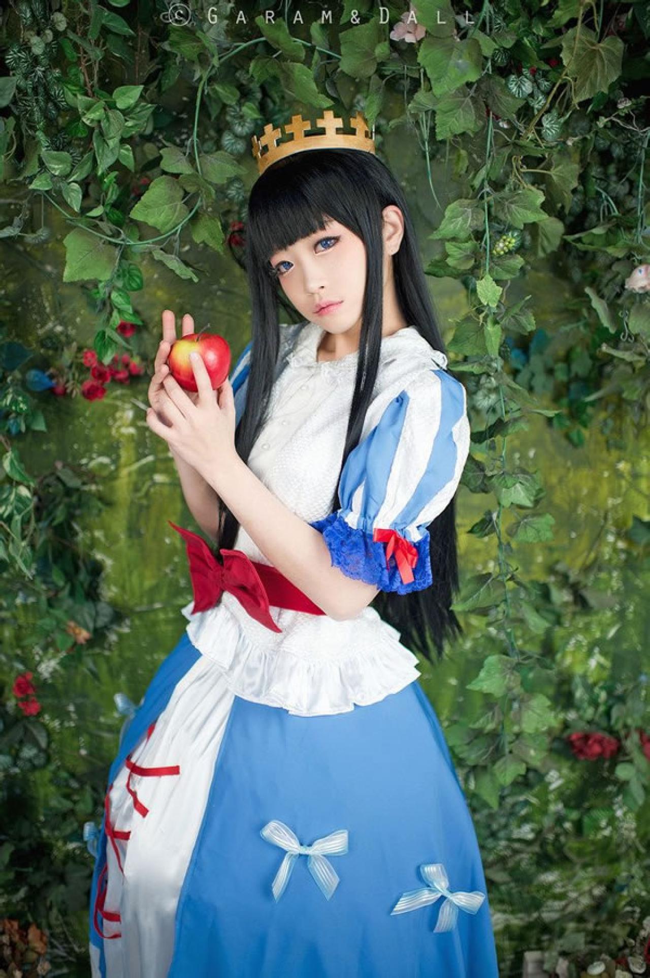 兔娘Tomia穿着蓝白洋装扮演白雪公主站在葡萄滕旁，双手轻轻抚摸着红苹果的侧面照
