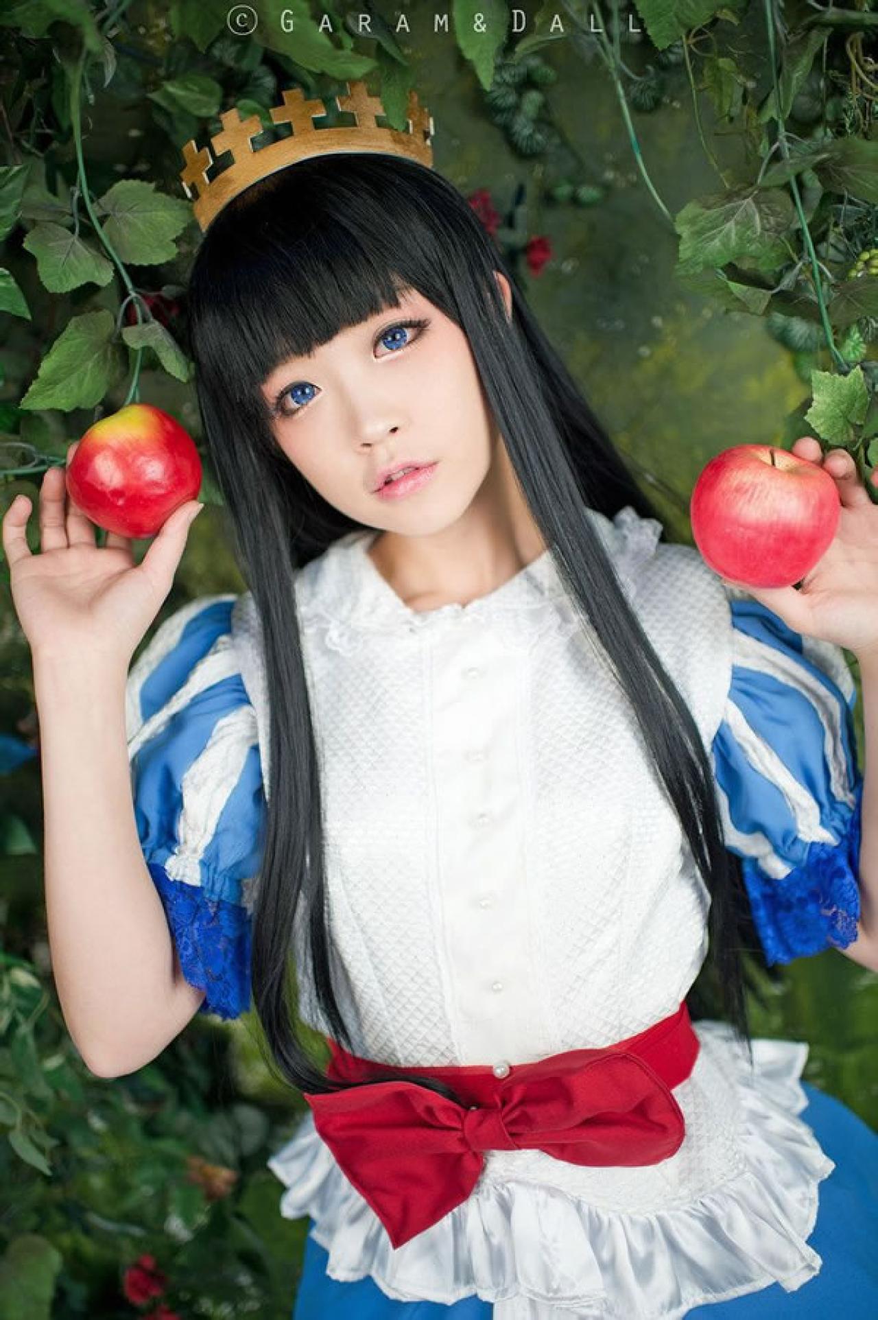 兔娘Tomia穿着蓝白洋装扮演白雪公主站在葡萄滕旁，两只手各拿一个苹果，举起的样子
