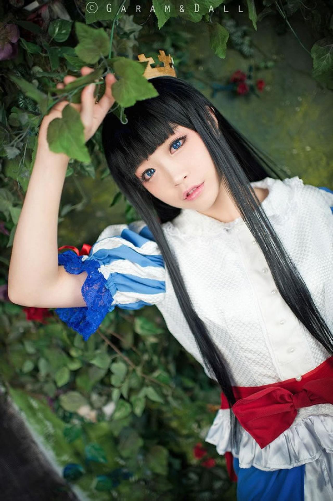 兔娘Tomia穿着蓝白洋装扮演白雪公主站在葡萄滕旁一手拽着葡萄藤叶，另一只手自然下垂的样子
