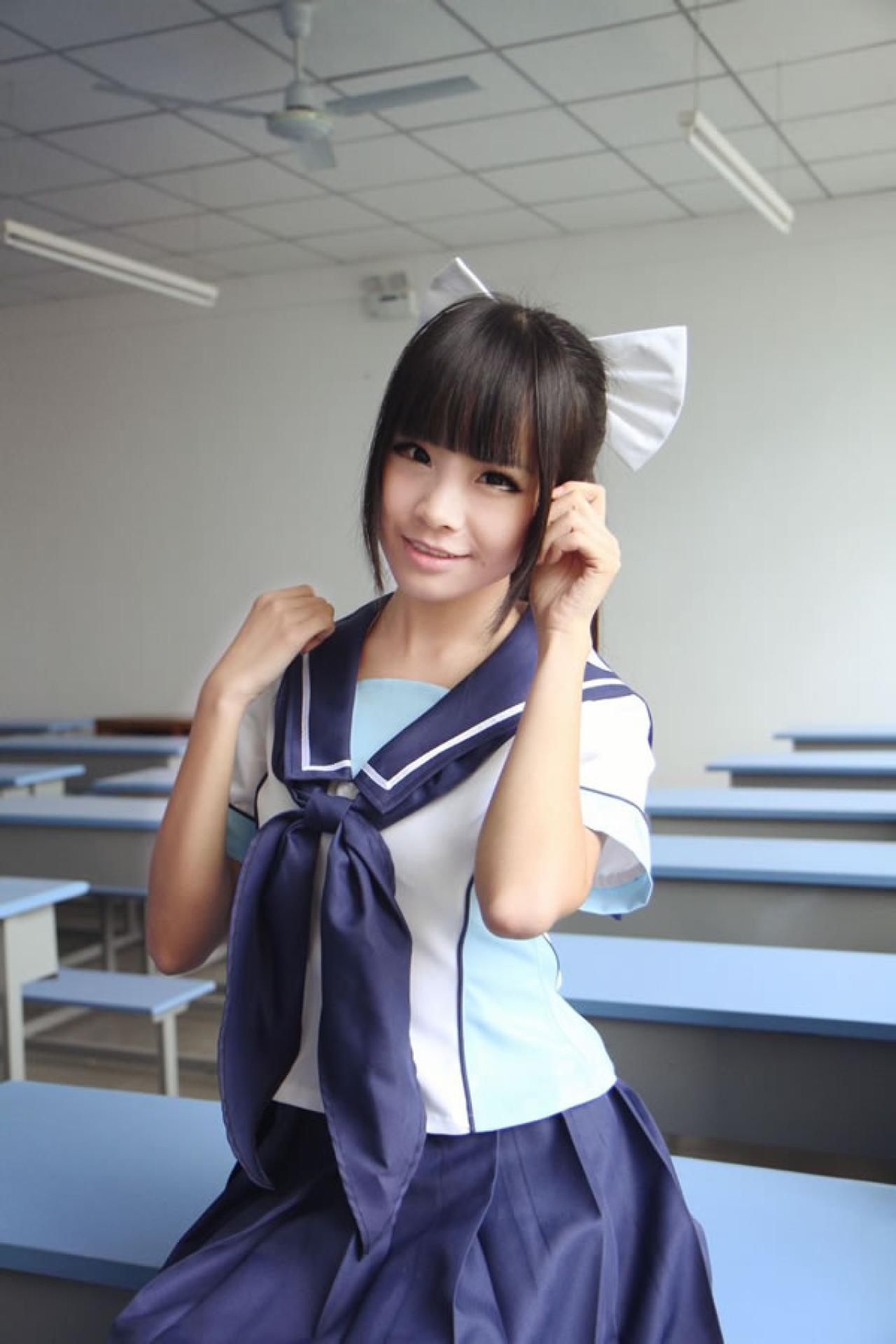 熊酱穿着蓝色学院校服扮演高岭爱花，一手扶肩，一手轻抚刘海儿坐在课桌上的样子