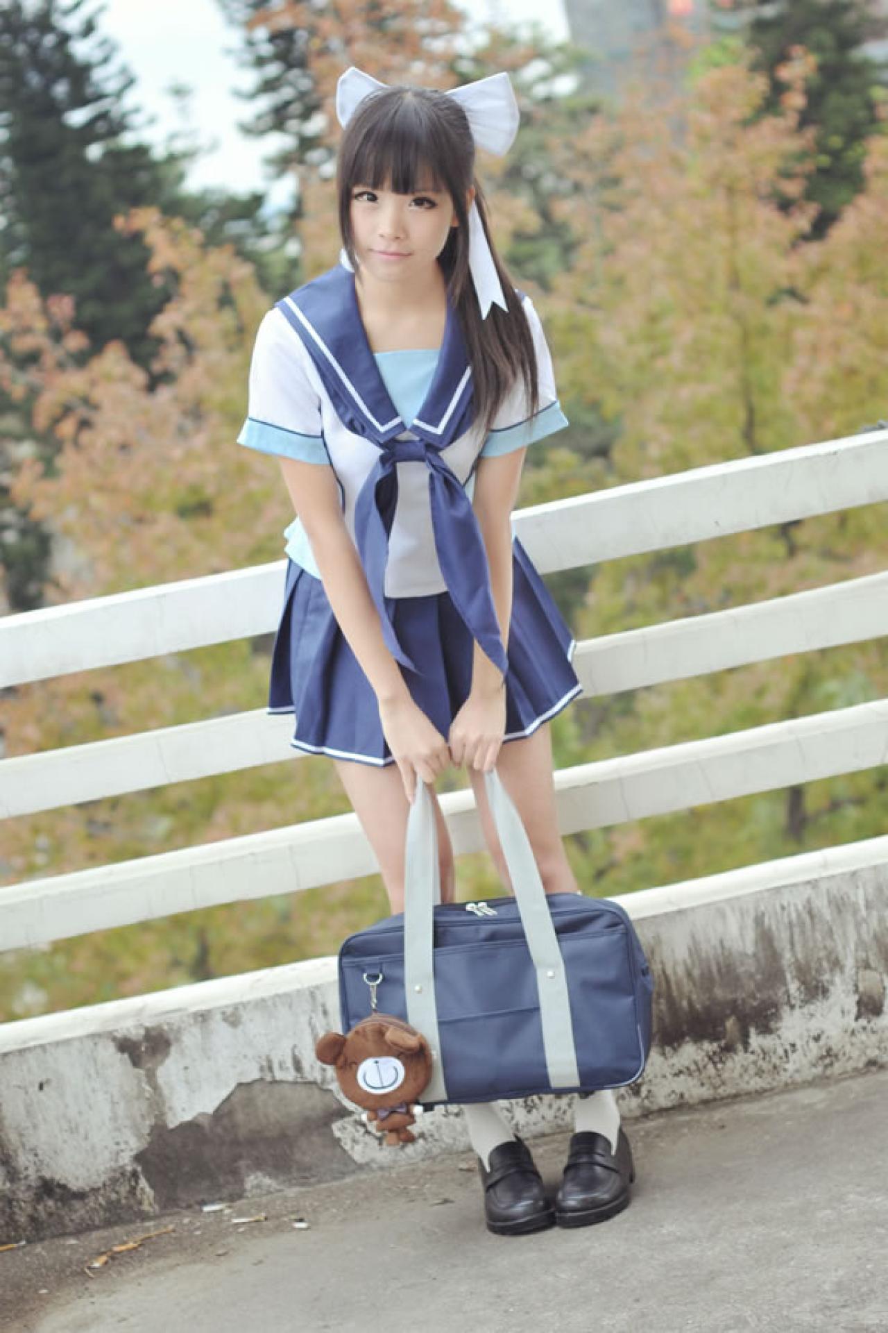 熊酱穿着蓝色学院校服扮演高岭爱花，提着挂着小熊玩具的包在天台上自然前倾身体的样子