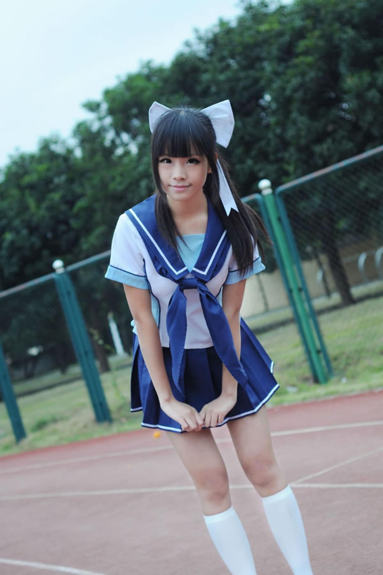 熊酱穿着蓝色学院校服扮演高岭爱花，右手拉着左手的食指，在操场跑道上，略微前倾身体