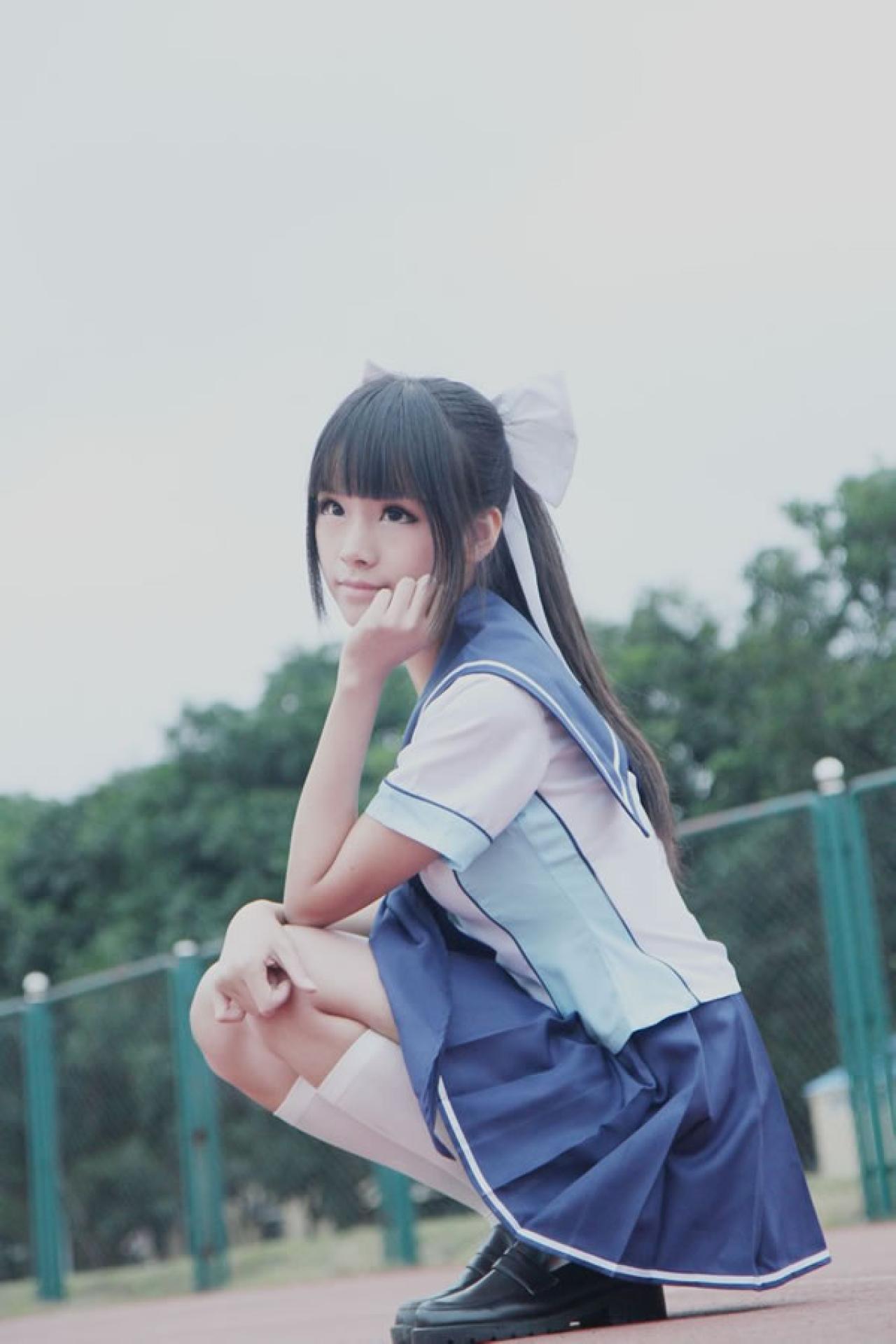 熊酱穿着蓝色学院校服扮演高岭爱花，蹲在操场跑道上，一只手搭在膝盖，另一只手扶着下巴