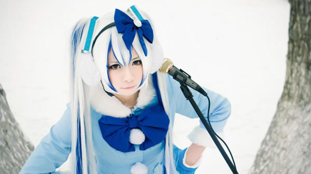 贤儿sherry穿着蓝色棉服扮演雪初音，站在雪地中把话筒靠在肩膀上