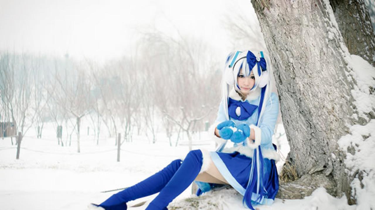 贤儿sherry穿着蓝色棉服扮演雪初音，靠在树干下，戴着手套搓着雪球