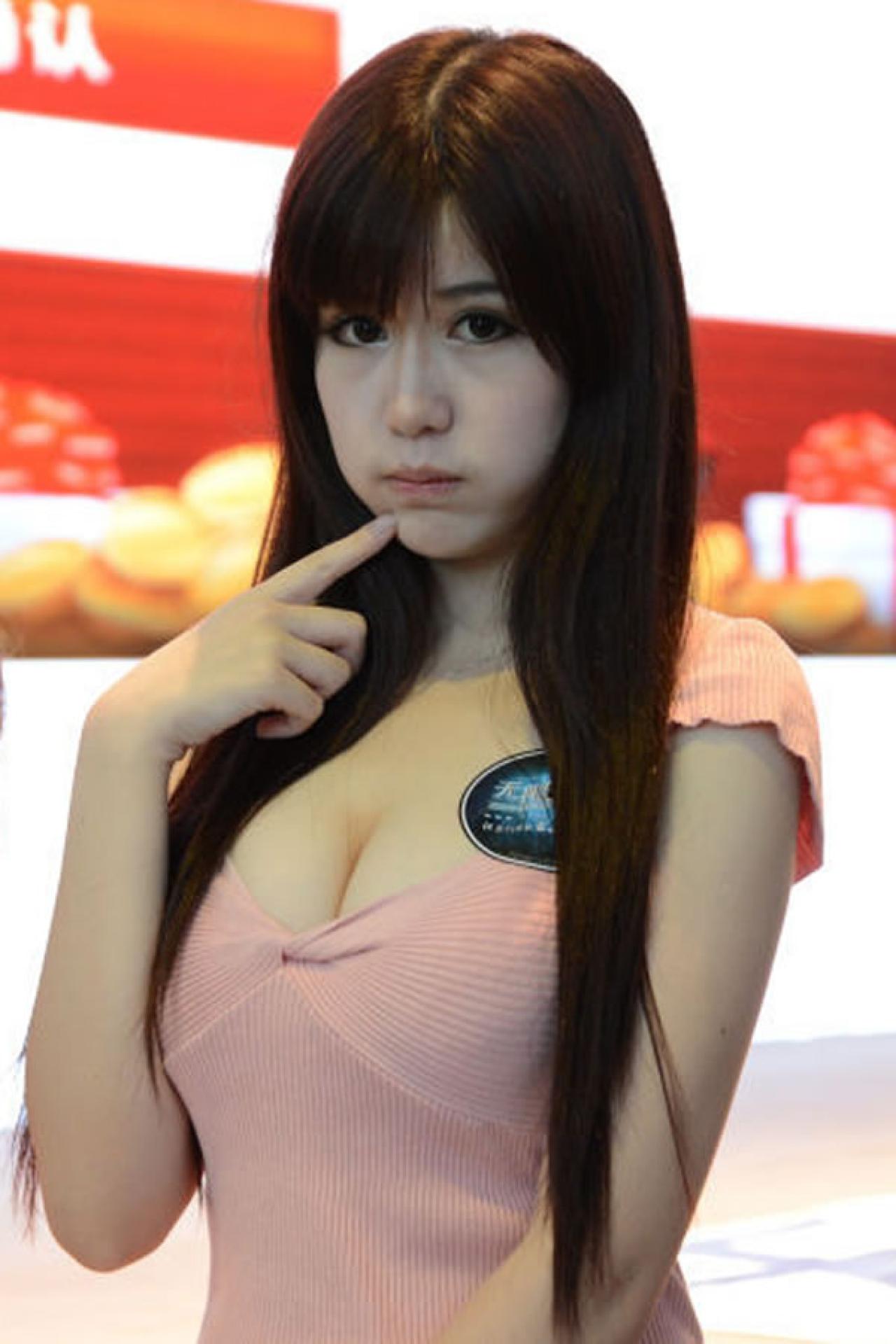 粉衣Showgirl站在展台，一手指着嘴，嘟嘴卖萌的上半身照