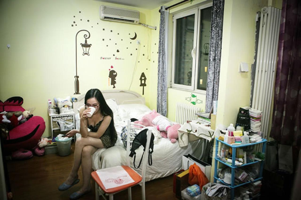 90后Showgirl王可欣杂乱的卧室，她本人正坐在卧室床沿喝水