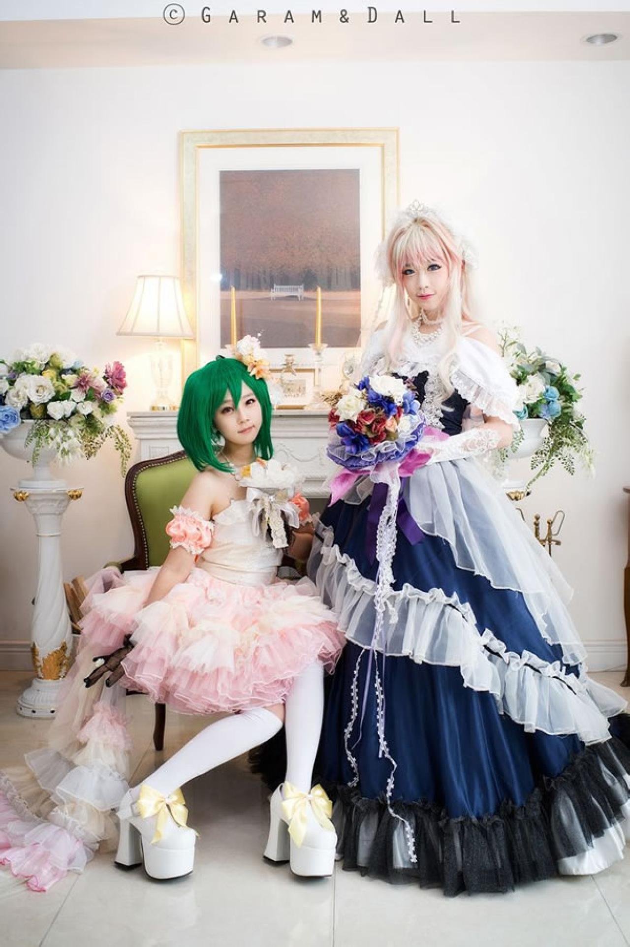 雪露·诺姆穿着蓝色洋装手捧鲜花战力和兰歌·李穿着粉色洋装坐在椅子上