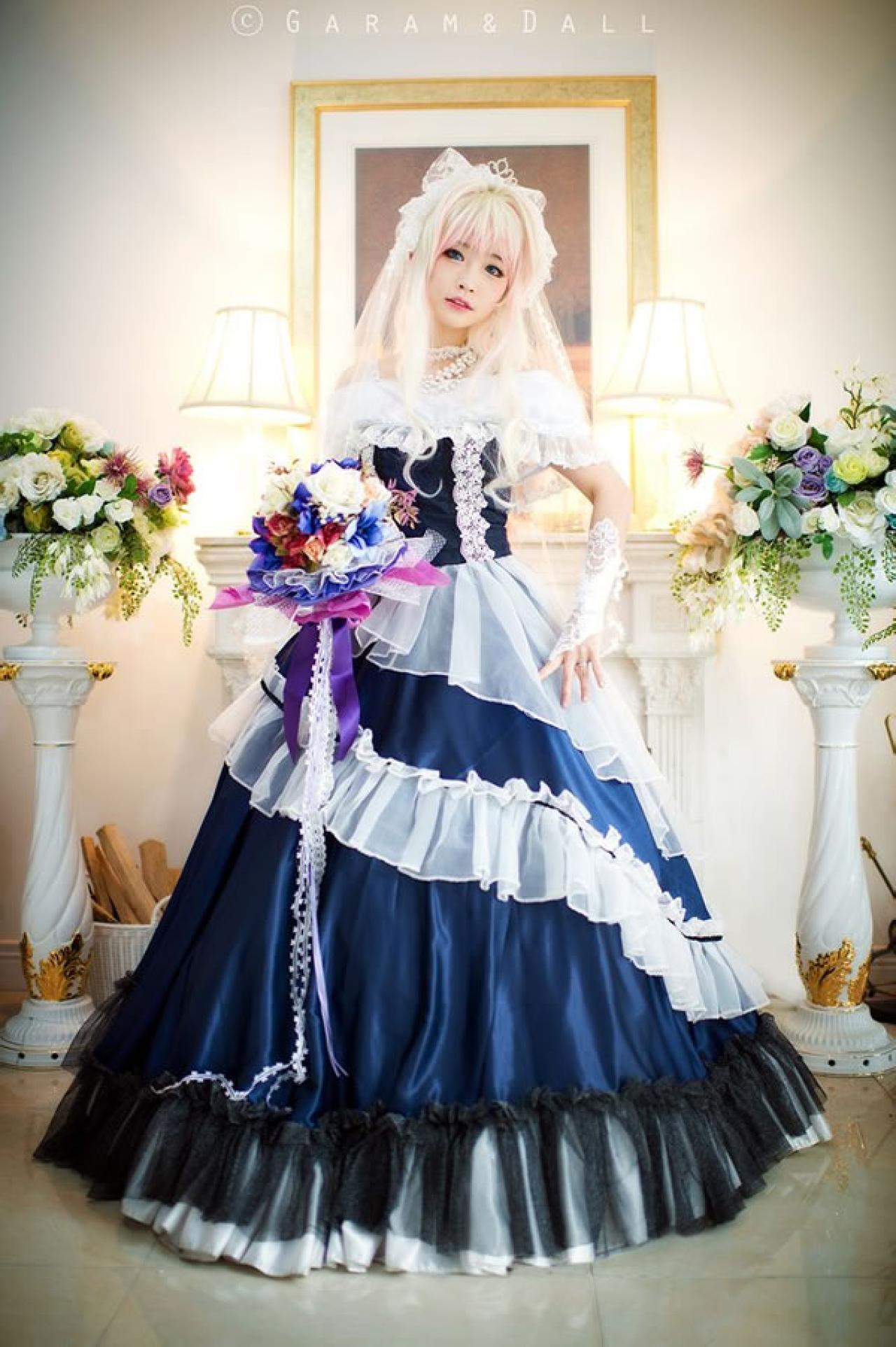 雪露·诺姆穿着蓝色洋装在台灯旁叉腰站立侧面