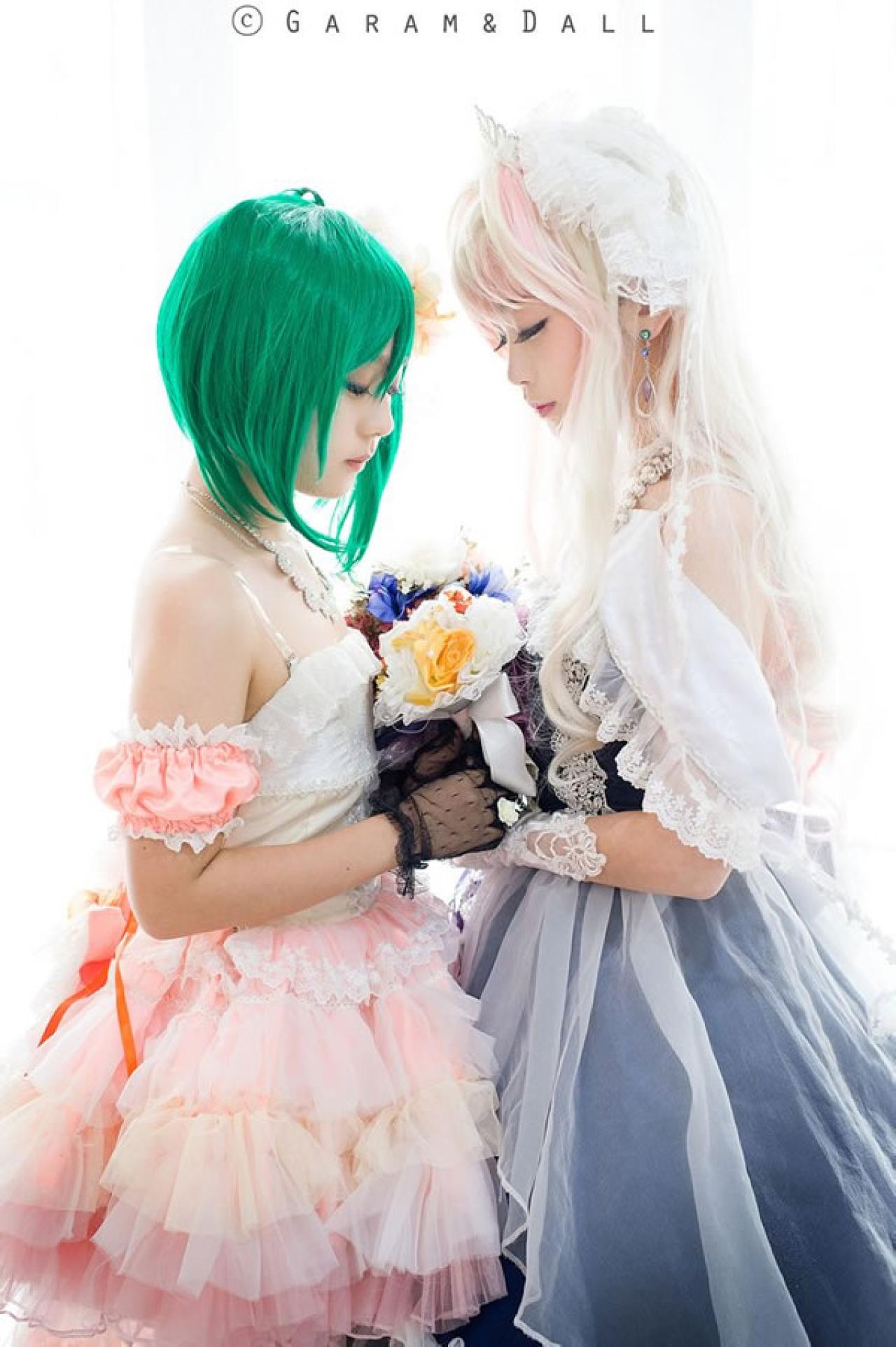 雪露·诺姆穿着蓝色洋装提着裙摆站在穿着粉色洋装的兰歌·李两人颔首捧着一束鲜花面对面站立