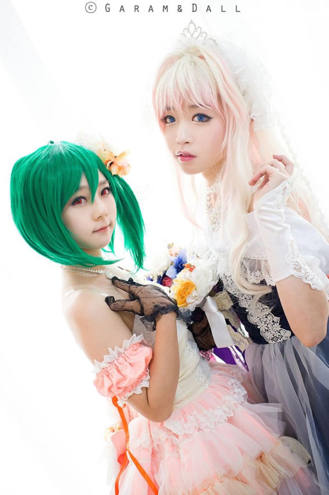 雪露·诺姆穿着蓝色洋装提着裙摆站在穿着粉色洋装的兰歌·李两人颔首捧着一束鲜花面对面镜头微微倾斜的抓拍