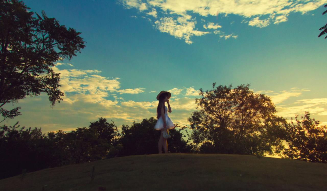 年糕扮演五更琉璃提起鞋子，走在青草地上，远处落日的余晖映红了半边碧蓝的天空。