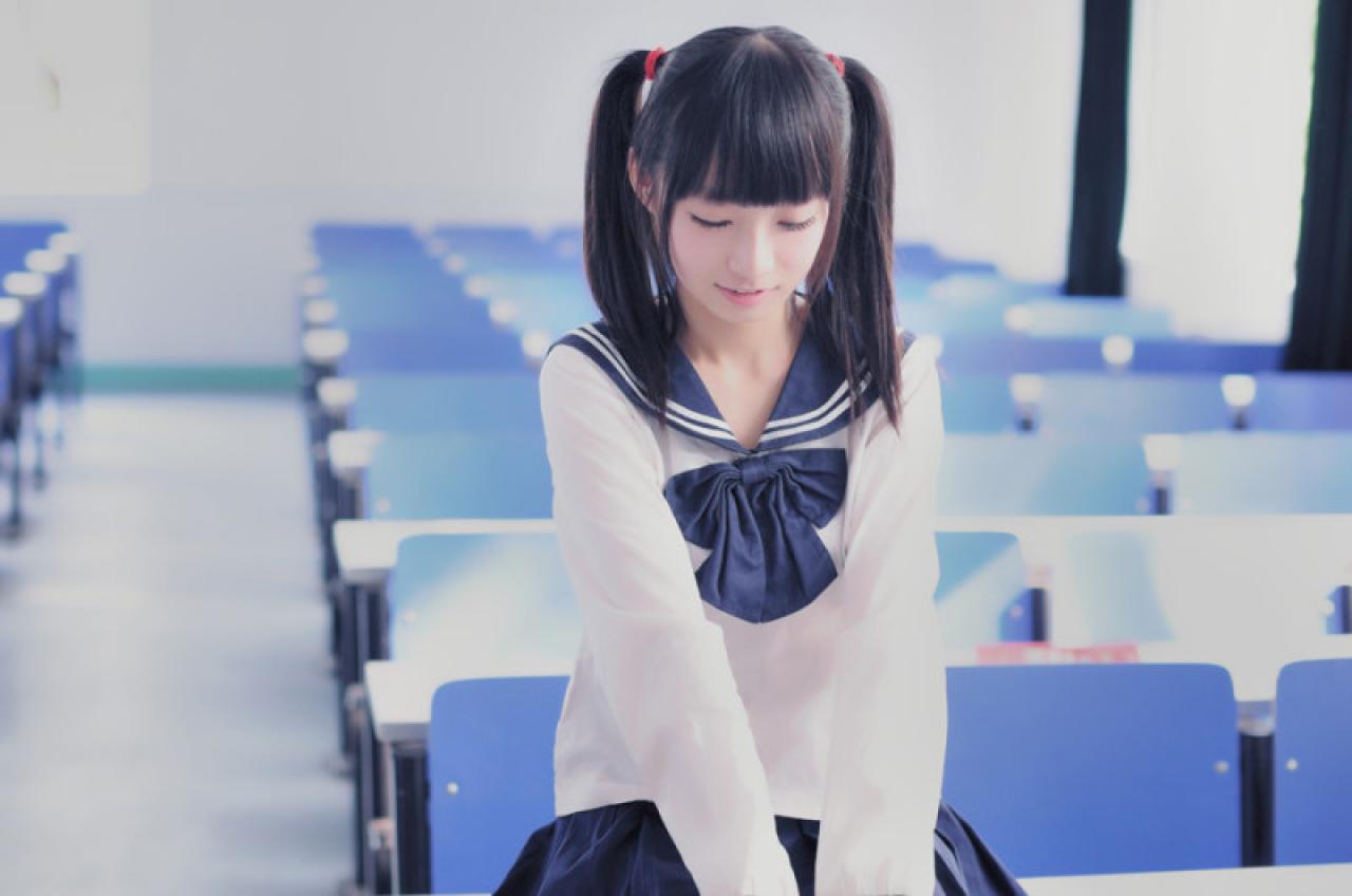 双马尾水手服少女坐在课桌上，双手放在膝盖上，低头想心事的样子