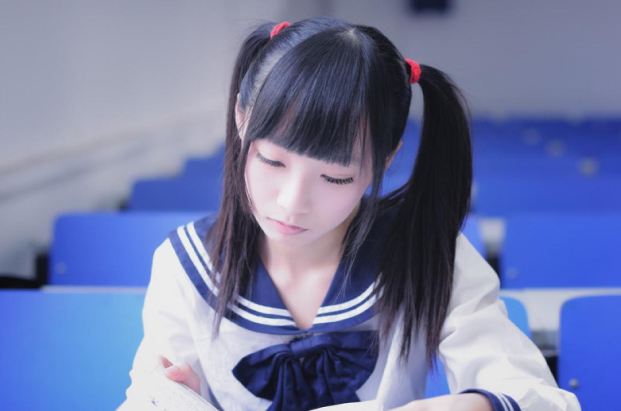 双马尾水手服少女正在课桌上专心翻阅书本的样子