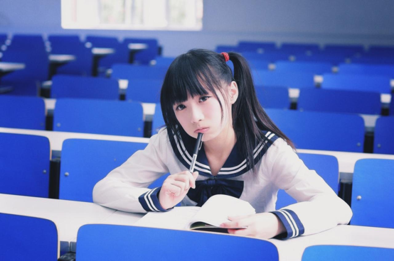 双马尾水手服少女用笔抵住下嘴唇，遇见难题时疑惑的神情。