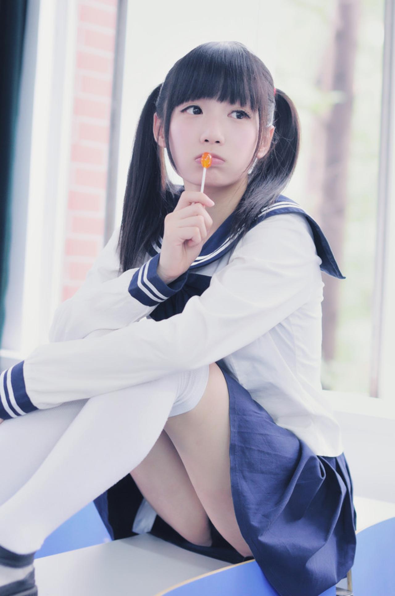 双马尾水手服少女侧身坐在课桌上，亲着棒棒糖回头仰望空空的座椅，有点失望的样子