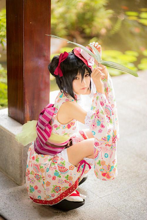 哀子扮演矢泽妮可蹲在亭子柱子旁，用三片芭蕉叶遮挡阳光