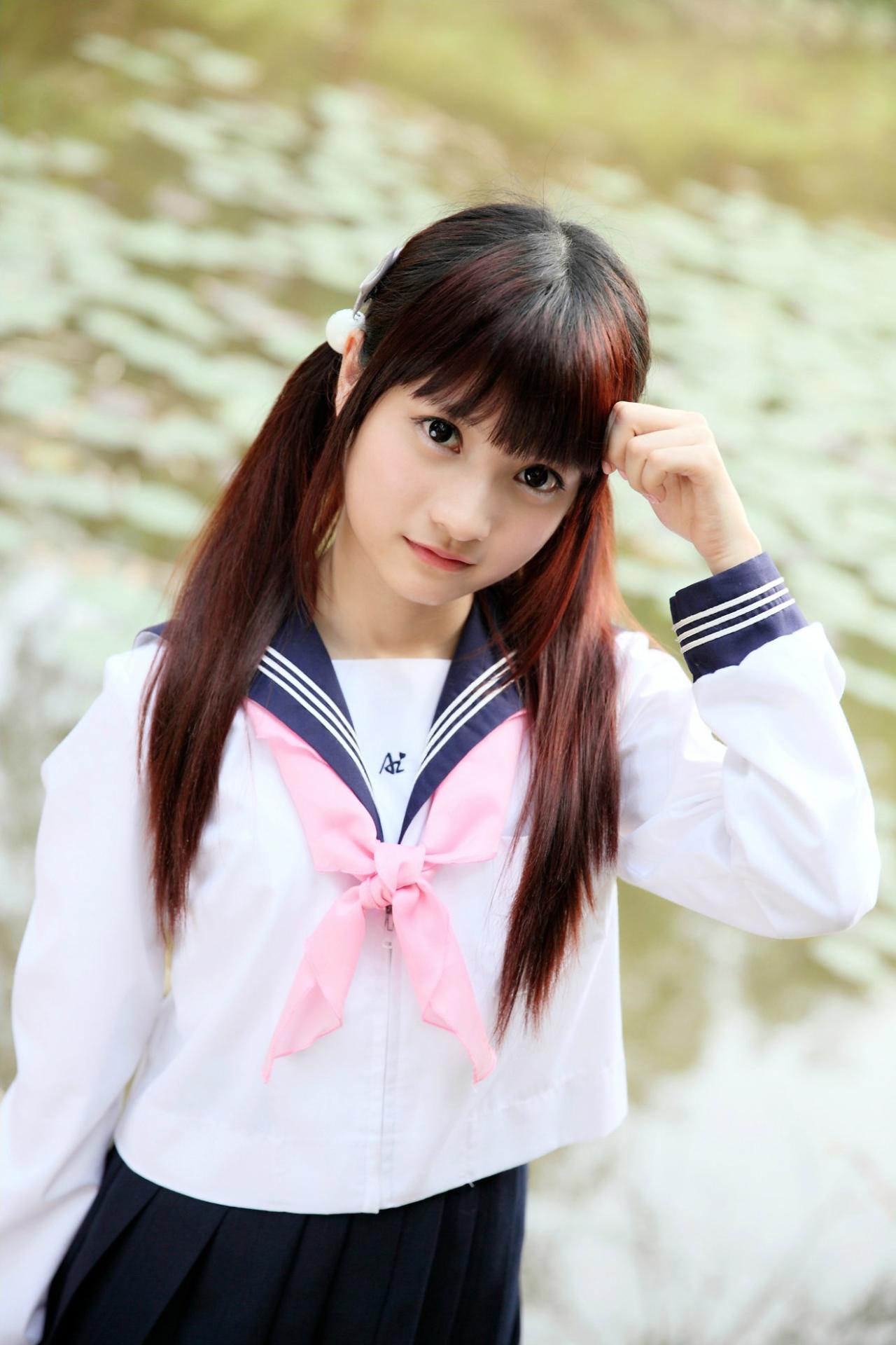 橘子酱穿着水手服站在河边，一只手半握拳捏着一撮刘海儿的姿势。