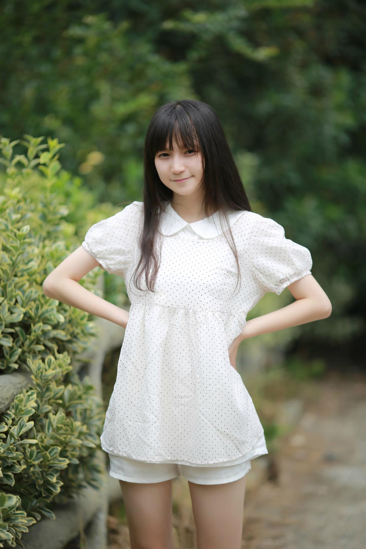 苏里柟穿着白色波点罩衫双手叉腰微笑站立的姿势