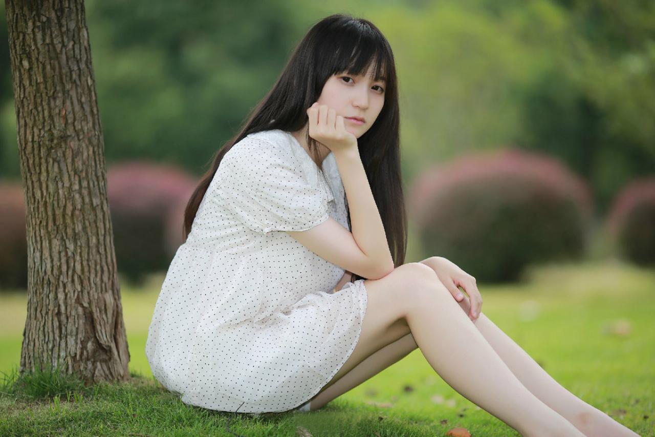 苏里柟穿着白色波点罩衫坐在树荫底下，双手放在膝盖上的姿势