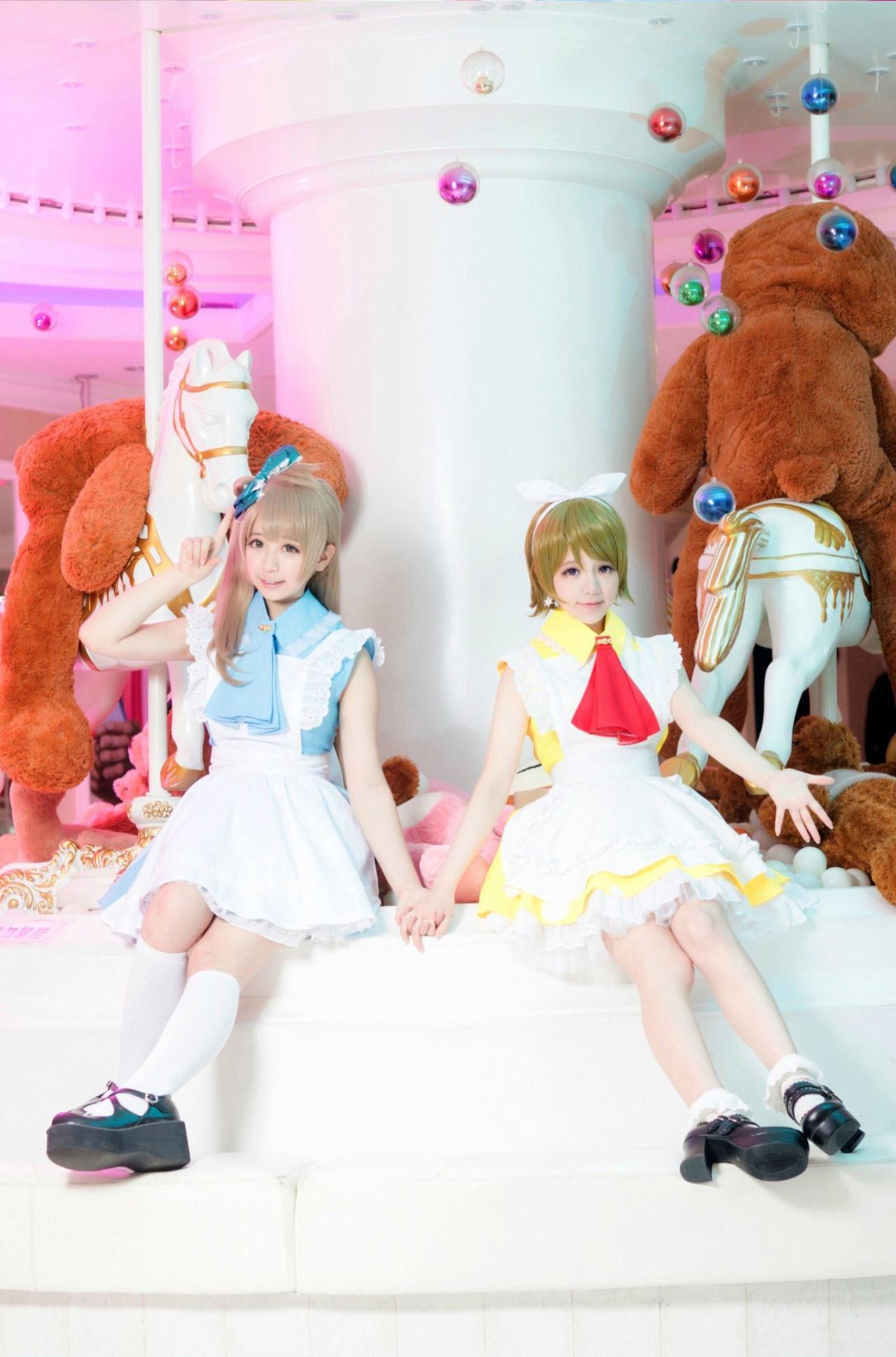 亚米_yami扮演的南小鸟和宝bA0_扮演小泉花阳手拉手坐在旋转木马上，南小鸟举起右手作八字手势，小泉花阳伸出左胳膊，五指张开