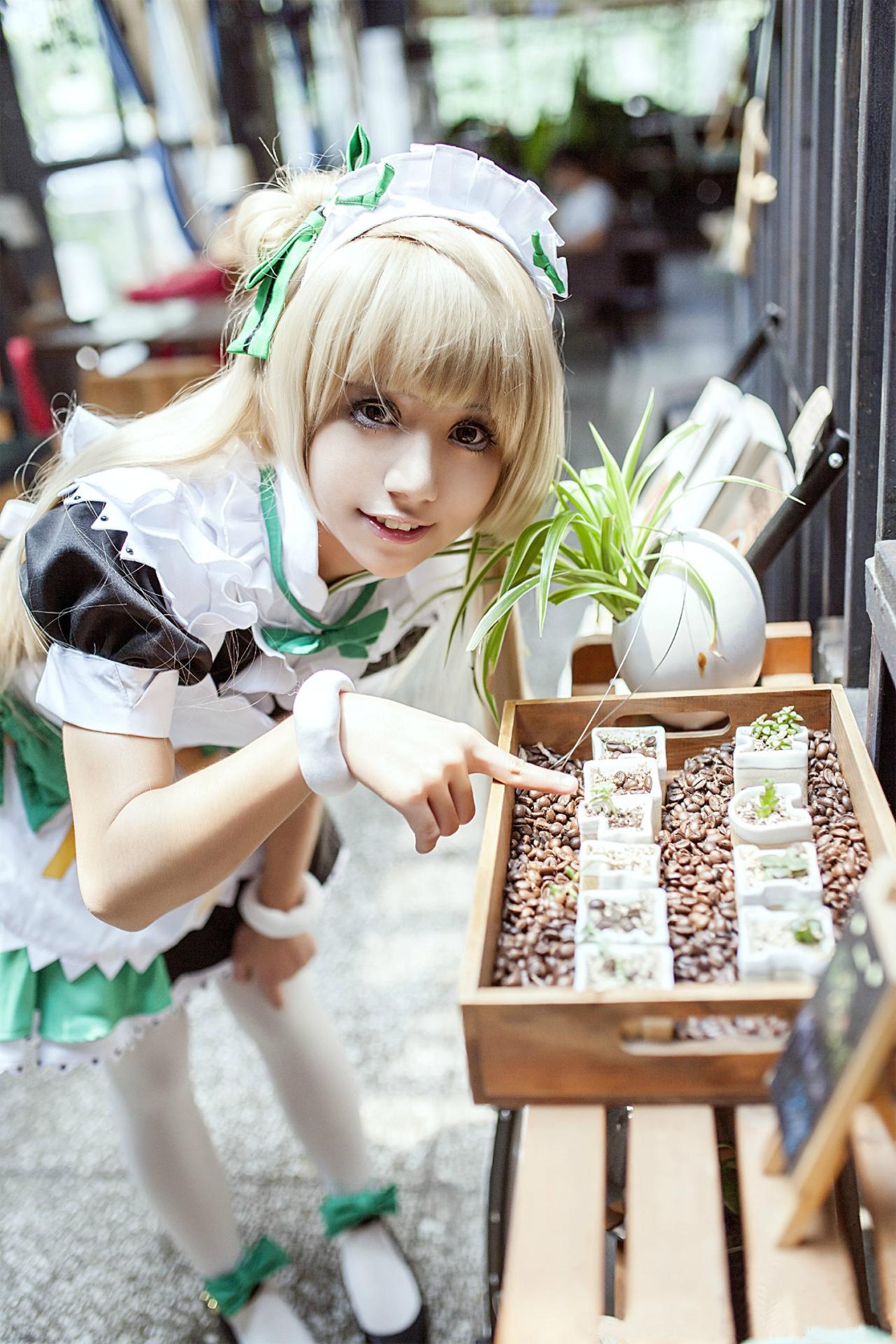 冰夜酱扮演南小鸟弯着腰，左手撑着膝盖，用右手食指指着正在萌发的嫩芽