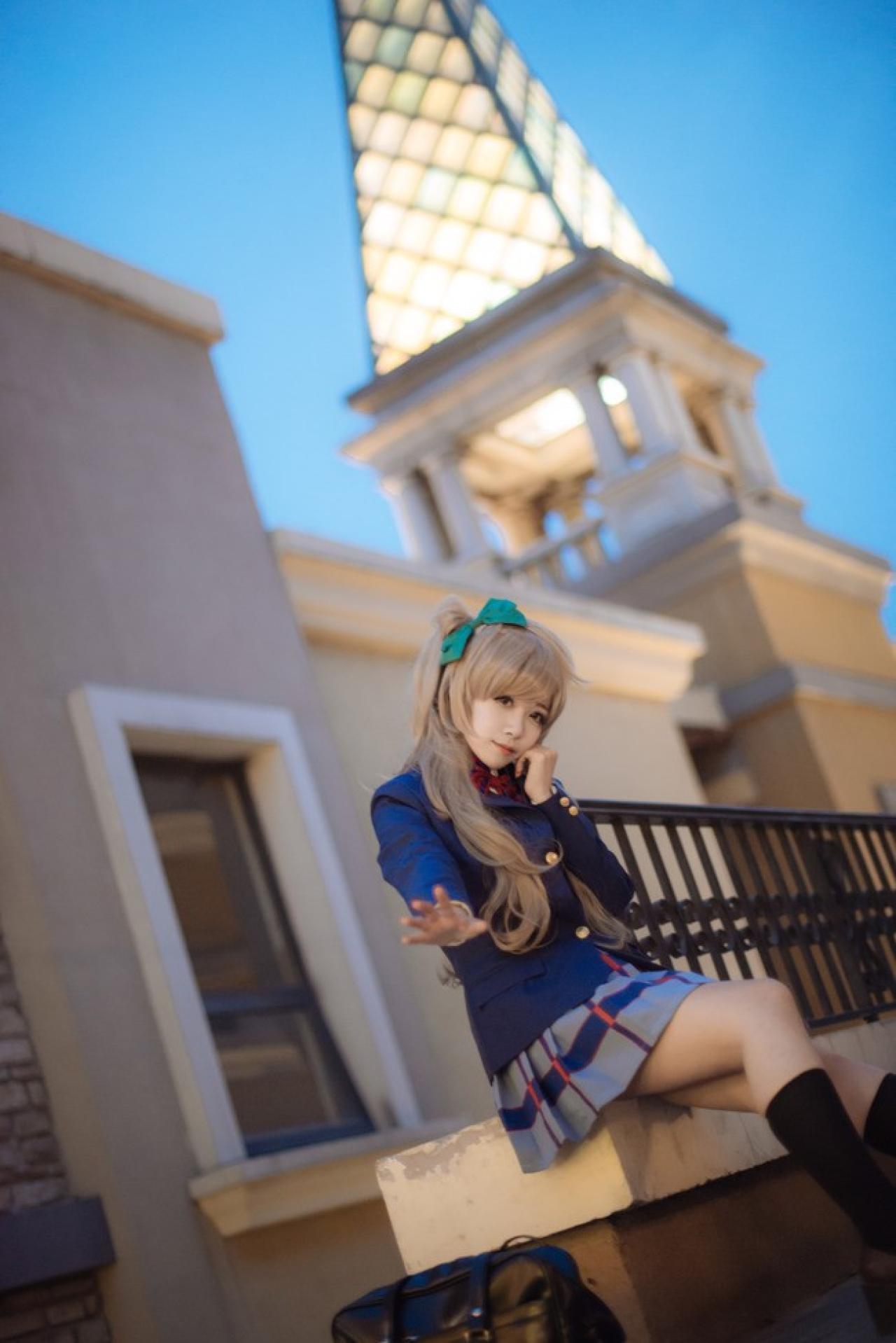 四月www扮演南小鸟坐在栏杆底部的台子上，左手半握拳撑着脸颊，右手伸展五指伸开的姿势